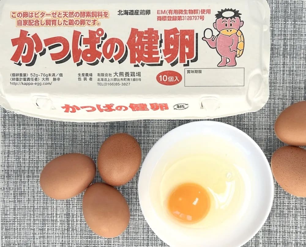 北海道・大熊養鶏場の「かっぱの健卵」のパッケージと、器に割り入れた生卵